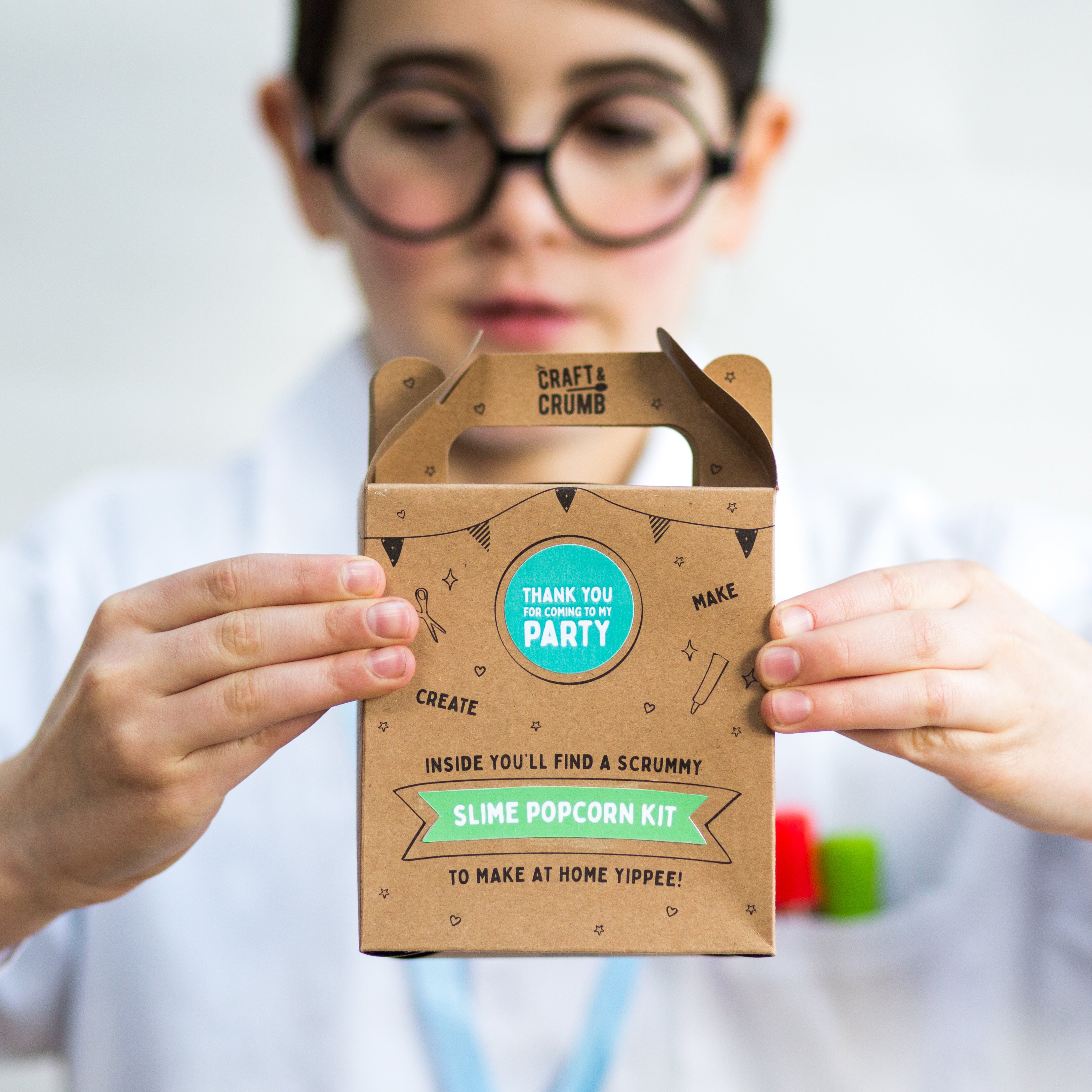 Child holding a "Slime Popcorn Kit" box, wearing glasses and a white shirt, focused on the packaging.